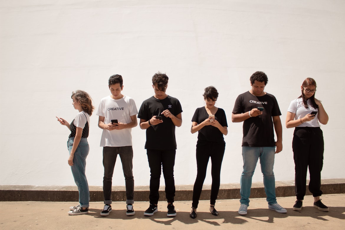Bilde viser seks ungdommer som alle står å kikker på mobiltelefonen sin.